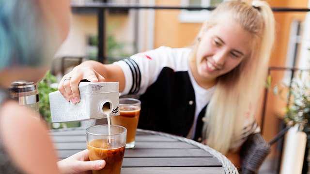 女子在户外咖啡馆向玻璃杯倒咖啡。